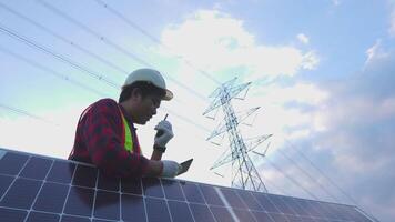 Ingenieria en estándar la seguridad uniforme trabajando inspeccionar el electricidad alto voltaje polo con tableta cerca torre con electricidad. video