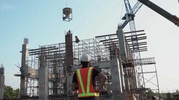 un civil ingenieros supervisa torrencial hormigón bomba en construcción sitio y puesta de sol antecedentes. video