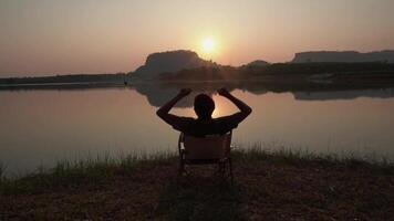 Back view of the shadow a young man and resting by the river mountain view at sunset. Success shadows successful people arms up. video