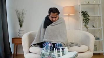 indiano doente homem com febre sentado embrulhado dentro uma xadrez em a sofá video