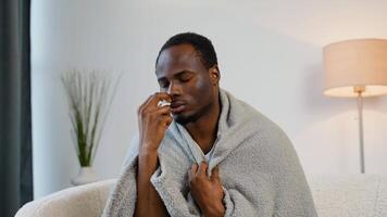 afrikanisch Mann Sprays ein Nasal- sprühen während Sitzung auf Sofa. Konzept von viral Krankheiten video