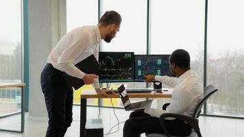 Two diverse traders, brokers in formalwear working using computers in the office video