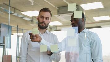 lluvia de ideas concepto. dos hombres reunión a oficina y utilizar enviar eso notas a compartir idea. pegajoso Nota en vaso pared video