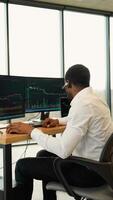 Concentrated african crypto trader sitting in front of computers, making professional analysis of candlestick chart, creating strategy. Vertical video