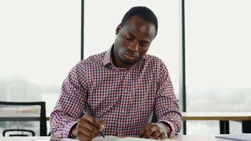 africano americano estudiante se sienta en biblioteca, preparar para examen y haciendo notas en cuaderno video