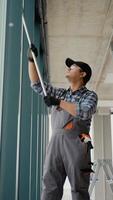 Indian man professional cleaning service worker in overalls cleans the pvc windows in office. Vertical video