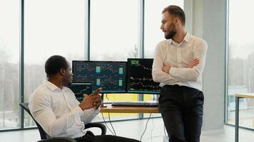 Two men traders at office together monitoring stocks data candle charts on screen video