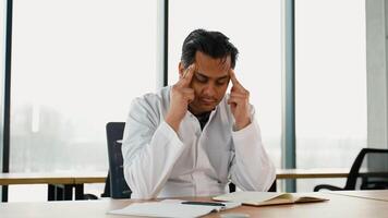 Stressed frustrated Indian doctor with headache sitting alone at work desk in hospital. Sad young gp feeling desperate and guilty for medical failure video