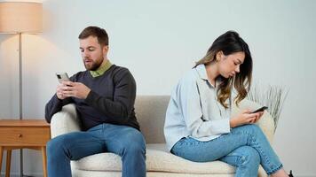 Mann und Frau, Paar, Familie Sitzung auf das Couch mit ihr Rücken zu jeder andere mit Telefone, tun nicht sich unterhalten zu jeder andere, tun nicht Zahlen Aufmerksamkeit, beschäftigt mit Telefone. Konflikt, Streit video