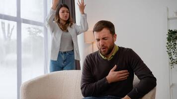 aggressivo donna urlando a impaurito marito a casa. un' uomo detiene su il suo il petto, sensazione cuore dolore. cuore attacco, miocardico infarto video