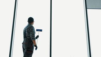 een Mens in uniform wast een ramen met schraper. professioneel huis of kantoor schoonmaak onderhoud video