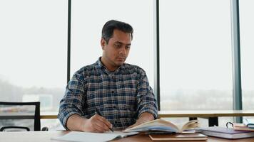 indio estudiante se sienta en biblioteca, preparar para examen y haciendo notas en cuaderno video