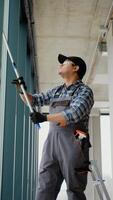 Indian man professional cleaning service worker in overalls cleans the pvc windows in office. Vertical video