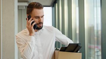 Employee found out by phone that he was fired. Fired worker with a box stands near the window video