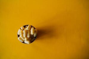 yellow corn sticks in a glass on a colored background, a full box of sweet corn sticks, a treat for children, yellow background, minimalism photo