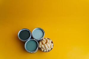 cans of paint on a colored background, shades of green, sweet corn lying in a can of paint, top view, minimalism concept, object on a yellow background close-up photo