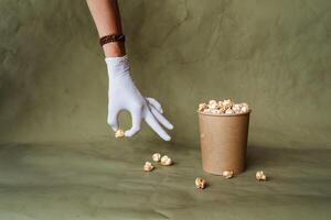 hand in a white glove reaches for popcorn, take food in protective gloves, hold a piece of food with two fingers, a full box of popcorn, security at the fast food distribution, minimal concept photo
