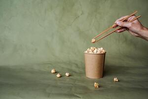 Chinese chopsticks to take popcorn from a box, a full can of popcorn, minimalistic style, on a colored background, concept picture, abstraction photo