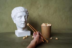 feed a plaster head with popcorn from a bucket, art concept, creativity, fast food and Chinese chopsticks photo