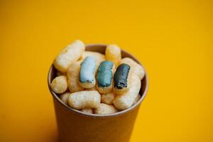 yellow corn sticks in a glass on a colored background, a full box of sweet corn sticks, a treat for children, yellow background, minimalism photo