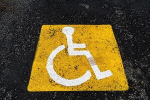 un amarillo firmar en el asfalto muestra un estacionamiento sitio para personas con discapacidades, para el desactivado, un la carretera firmar, marcas en el la carretera foto