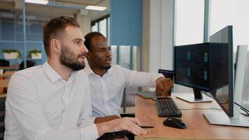 Two crypto traders sitting of computers, making professional analysis of candlestick chart, creating strategy, holding pen and notepad, looking at monitor video