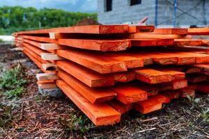 pine boards painted with red stain, lumber for construction are lying on the ground, long floor boards are stacked photo