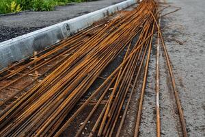 rebar for construction is lying on the asphalt, a pile of rusty rods, metal rods orange color photo