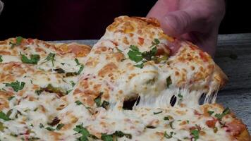 detailopname van mensen handen nemen plakjes pizza. kader. duurt aan het eten een plak van pizza met kaas, tomaten en ham. heerlijk voedsel voor gulzigheid en genot. langzaam beweging Mens duurt een deel van heet video