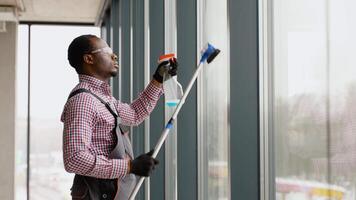 Black man professional cleaning service worker in overalls cleans the pvc windows in office video
