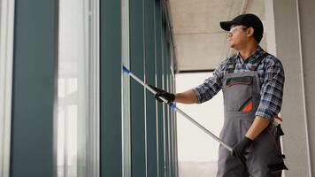 A man in uniform washes a windows with scraper. Professional home or office cleaning service video