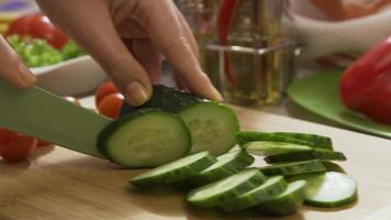 Close up of hand with knife cutting cucumbers on wooden board. Scene. Fresh cucumber on a wooden cutting board. Close up shot of whole cucumber, arrangement or pile. Salad preparation - cutting video