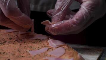 cucinando Pizza lento movimento. telaio. fabbricazione Pizza con formaggio, pomodoro incolla, salsiccia e mostarda. il opera di il cucinare. il cucinare organizza pezzi di salsiccia e Pizza con formaggio e pomodoro incolla. pieno video