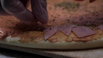 Hände vorbereiten ein Pizza. rahmen. Koch im das Küche Putten das Zutaten auf das Pizza. Pizza Konzept. Produktion und Lieferung von Lebensmittel. Nahansicht Hand von Koch Bäcker im Weiß Uniform Herstellung Pizza beim video