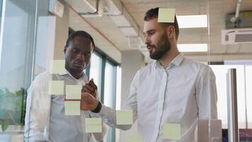 Brainstorming Konzept. zwei Männer Treffen beim Büro und verwenden Post es Anmerkungen zu Teilen Idee. klebrig Hinweis auf Glas Mauer video