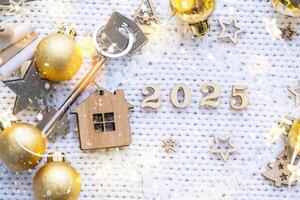 House key with keychain cottage on festive background with stars, lights of garlands. New Year 2025 wooden letters, greeting card. Purchase, construction, relocation, mortgage, insurance photo