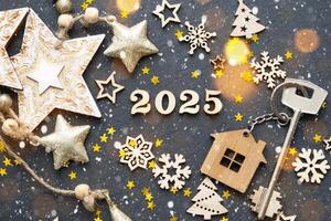 casa llave con llavero cabaña en festivo negro antecedentes con estrellas, luces de guirnaldas nuevo año 2025 de madera letras, saludo tarjeta. compra, construcción, reubicación, hipoteca, seguro foto