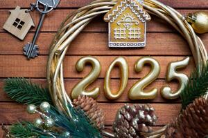 New Year House key with keychain cottage on festive brown wooden background with number 2025 in wreath, lights of garlands. Purchase, construction, relocation, mortgage, insurance photo