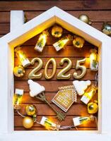House key with keychain cottage on festive brown wooden background with stars, lights of garlands. New Year 2025 golden letters under the roof. Purchase, construction, relocation, mortgage, insurance photo