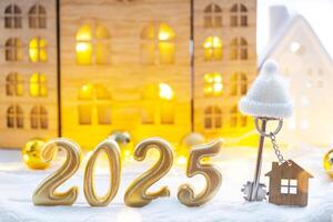 Golden figures number 2025, key and tiny home on background of cozy windows of a house with warm light with festive decor of stars,snow and garlands. Greeting card, Happy New Year, cozy home photo