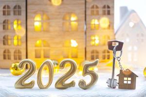 Golden figures number 2025, key and tiny home on background of cozy windows of a house with warm light with festive decor of stars,snow and garlands. Greeting card, Happy New Year, cozy home photo