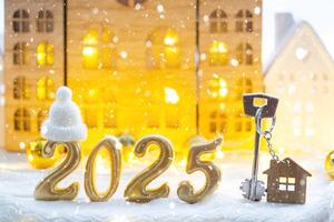 Golden figures number 2025, key and tiny home on background of cozy windows of a house with warm light with festive decor of stars,snow and garlands. Greeting card, Happy New Year, cozy home photo