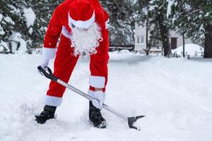 Papa Noel claus limpia nieve con pala en invierno al aire libre después un nevada. limpieza el calles en el aldea, claro el paso para carros, difícil clima condiciones para Navidad y nuevo año foto