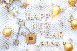 House key with keychain cottage on festive background with stars, lights of garlands. New Year 2025 wooden letters, greeting card. Purchase, construction, relocation, mortgage, insurance photo