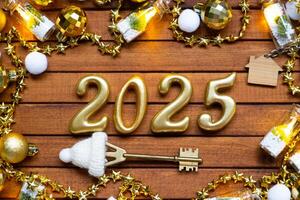 House key with tiny figure of home mock up on festive brown wooden background, lights of garlands. New Year 2025 wooden letters, greeting card. Purchase, construction, relocation, mortgage, insurance photo