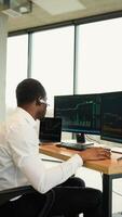 Black trader or businessman in formal wear working with charts and market reports on computer screens in his modern office. Vertical video