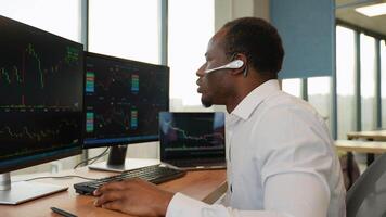 Concentrated african crypto trader sitting in front of computers, making professional analysis of candlestick chart, creating strategy video