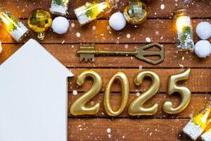 House key with tiny figure of home mock up on festive brown wooden background, lights of garlands. New Year 2025 wooden letters, greeting card. Purchase, construction, relocation, mortgage, insurance photo