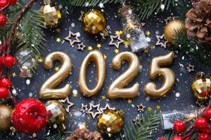 The golden figures 2025 made of candles on a black stone slate background are decorated with a festive decor of stars, sequins, fir branches, balls and garlands. Greeting card, happy New Year. photo