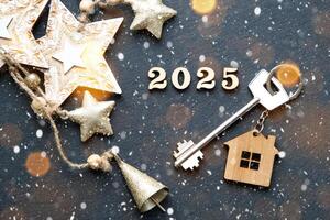 House key with keychain cottage on festive black background with stars, lights of garlands. New Year 2025 wooden letters, greeting card. Purchase, construction, relocation, mortgage, insurance photo